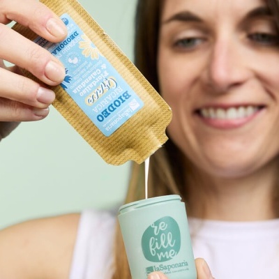 Mulher a verter líquido de saquinho para copo com texto