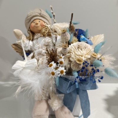 Boneco decorativo com flores secas e fita azul em superfície branca
