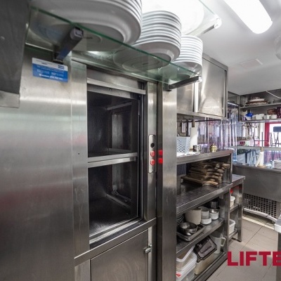 Cozinha industrial com forno metálico grande e prateleiras com pratos brancos