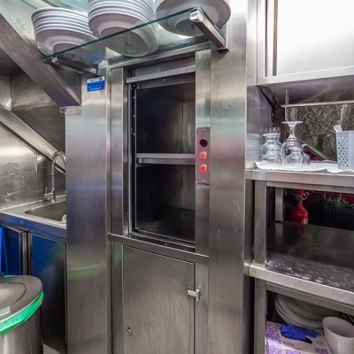 Elevador de pratos de aço inoxidável com pratos brancos e prateleiras metálicas em cozinha profissional