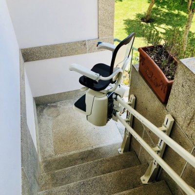 Cadeira elevatória branca e preta numa escada exterior de pedra com vaso e jardim ao fundo