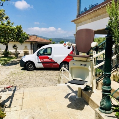 Elevador de cadeira motorizada instalada em escadaria exterior com carrinha de serviço ao fundo e logótipo LIFTECH.