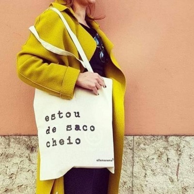 Pessoa com casaco amarelo segurando sacola de tecido branca com frase estampada