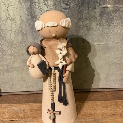 Estatueta de cerâmica de homem religioso segurando uma criança, com terço e crucifixo, sobre superfície de madeira