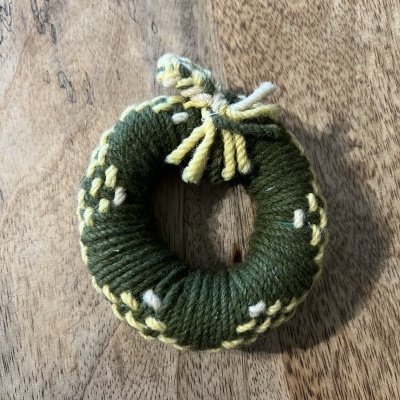 Elástico redondo de fio trançado verde, amarelo e bege sobre madeira.