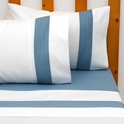 Roupas de cama brancas e azuis em cama com cabeceira de madeira