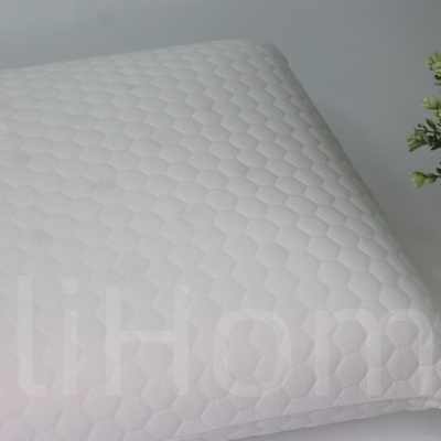 Travesseiro branco acolchoado com padrão de colmeia próximo a vaso dourado com planta