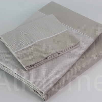 Conjunto de roupa de cama bege com riscas finas brancas dobrado sobre superfície clara