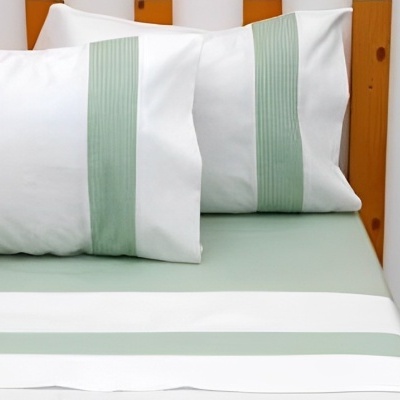 Conjunto de cama com lençol verde e almofadas brancas com faixa verde numa cama com estrutura de madeira.