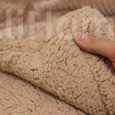 Tecido felpudo bege com textura tipo lã de ovelha sendo segurado por uma mão