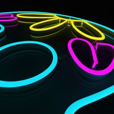 Letreiro luminoso em neon azul, amarelo e rosa com formas circulares e padrão de folha.