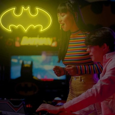 Jovens a jogar em máquinas de arcade com símbolo do Batman iluminado ao fundo