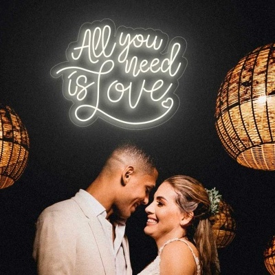 Casal sorridente sob candeeiros de vime com frase luminosa All you need is Love