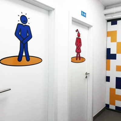 Portas brancas com símbolos de homem e mulher e padrão geométrico colorido na parede