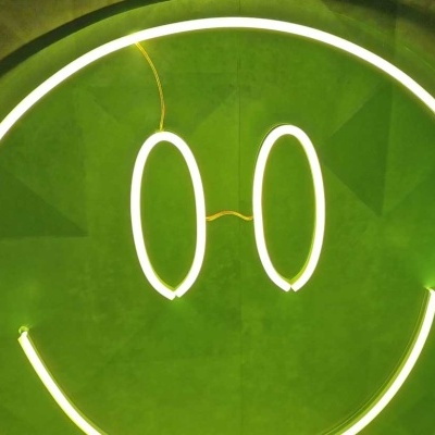 Placa de néon smiley branca numa parede verde