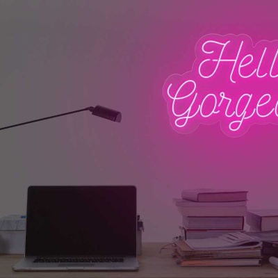 Mesa de trabalho com computador portátil, livros, candeeiro e letreiro de néon rosa