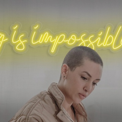 Frase em neon amarelo numa parede e mulher com cabelo curto sentada