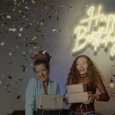 Dupla de mulheres a segurar presentes em ambiente festivo com letreiro Happy Birthday