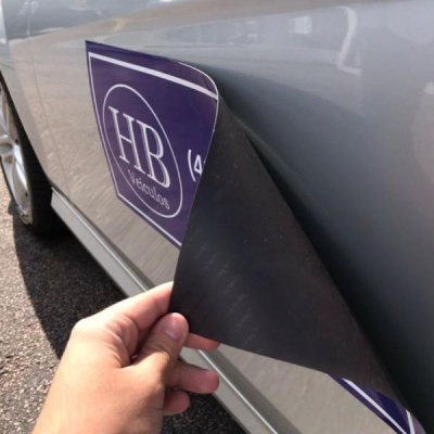 Adesivo roxo e branco com texto 'HB Veículos' na lateral de um carro cinzento prateado