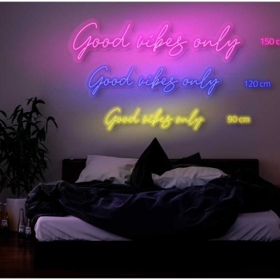 Quarto escuro com cama preta e branca, planta, mesa de cabeceira e letreiros de néon coloridos na parede