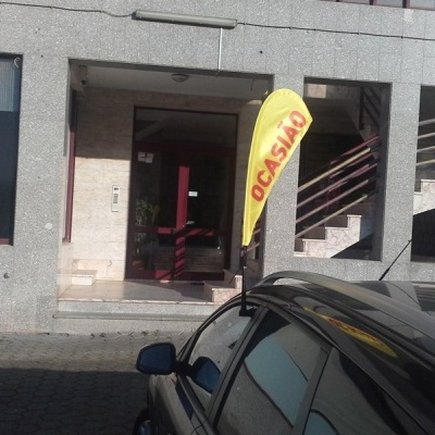 Entrada de prédio com bandeira amarela 'OCASIÃO' e carro preto estacionado