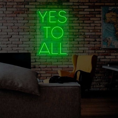 Cadeira amarela e sofá cinza numa sala com parede de tijolos à vista e neon YES TO ALL