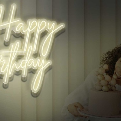 Letreiro de néon 'Happy Birthday' na parede, mulher segurando bolo