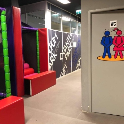 Porta de casa de banho com sinal WC e figuras azul e vermelha num corredor com proteções coloridas e parede decorada