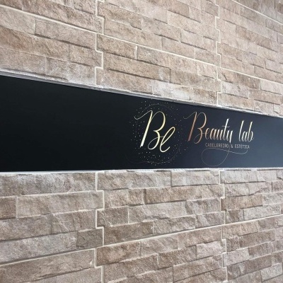 Placa preta com texto dourado e branco numa parede de tijoleira bege