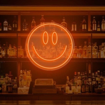 Prateleira de bar com garrafas de bebidas e símbolo de rosto sorridente em néon laranja.