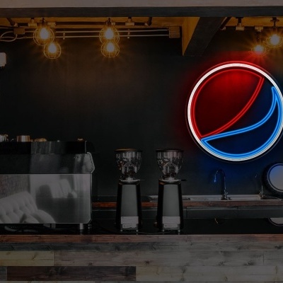 Balcão de bar com máquinas de café e neon com logotipo da PEPSI