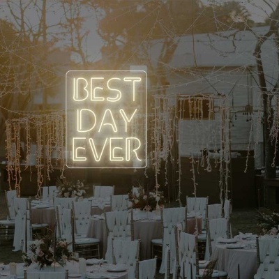 Espaço ao ar livre decorado com mesas, cadeiras brancas e letreiro luminoso BEST DAY EVER.