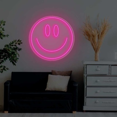 Sala com sofá preto, cómoda branca, planta, candeeiro e luz de néon rosa sorridente na parede