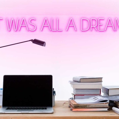 Mesa de escritório com laptop, lâmpada, livros e texto em néon rosa na parede