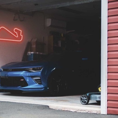 Carro desportivo azul escuro dentro de uma garagem com porta aberta e luz de néon vermelha na parede