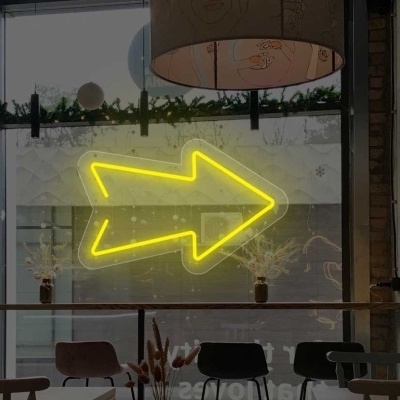 Mesa e cadeiras em espaço interior com parede de tijolos e seta amarela em néon na janela