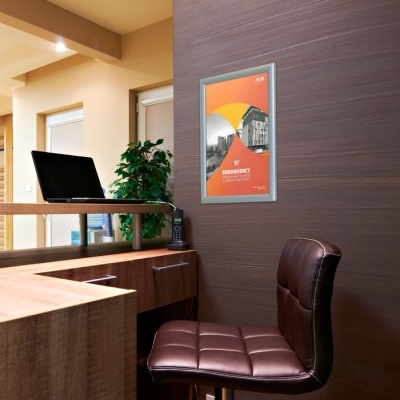 Escritório com cadeira de couro castanho, secretária de madeira, monitor, telefone e cartaz laranja na parede