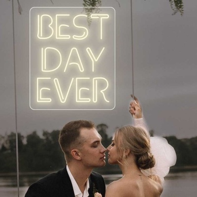 Neon com texto 'BEST DAY EVER' branco ao ar livre com casal formal