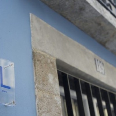 Placa de vidro com letras AL e texto Apartamentos Lisboa numa parede azul perto de porta com moldura de pedra
