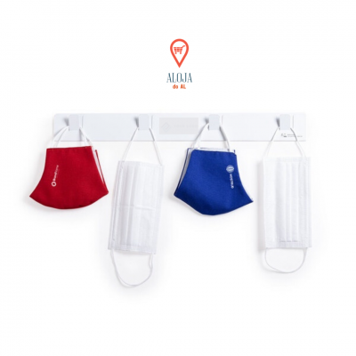 Quatro máscaras penduradas num suporte branco, duas de tecido vermelha e azul com texto, e duas cirúrgicas brancas