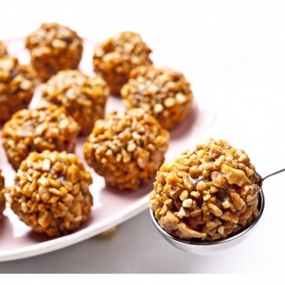 Trufas cobertas com pedaços de nozes em prato rosa e uma trufa numa colher de metal.