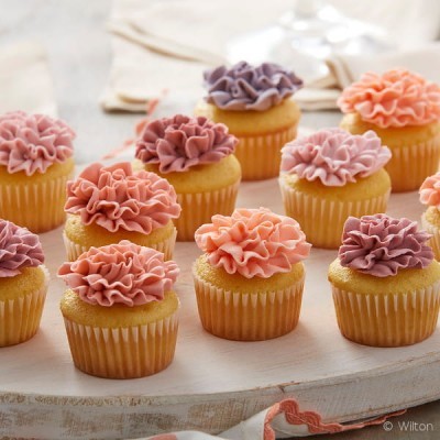 Doze cupcakes com cobertura de creme em tons de roxo, rosa e coral, com decoração em forma de flores.