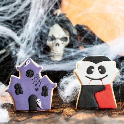 Biscoitos decorados de Halloween em forma de casa mal-assombrada e vampiro sobre tecido preto e teias falsas