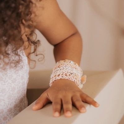 Pulseira de crochê branca e cor de pêssego no pulso de criança com vestido branco