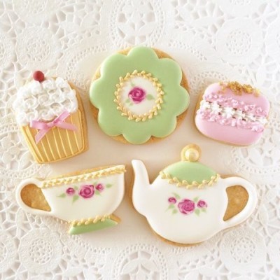 Bolachas decoradas com glacê em forma de cupcake, flor, chávena e bule, com decoração floral e detalhes coloridos