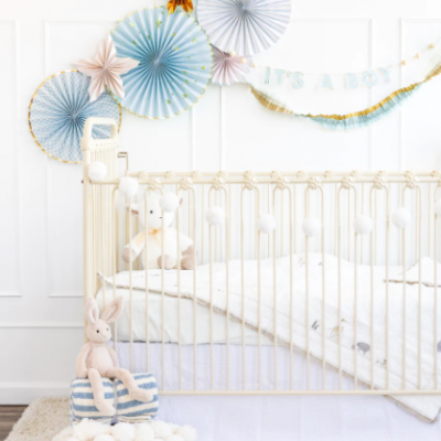 Berço creme decorado para bebé com peluches e leques azuis e dourados na parede