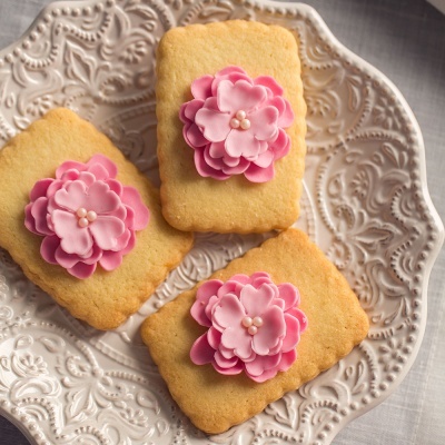 Bolachas decoradas com flores de açúcar cor-de-rosa num prato branco com relevo