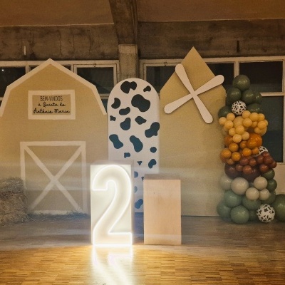 Decoração temática com celeiro, arco de balões, trator verde, número iluminado 2 e carrinho de mão com palha