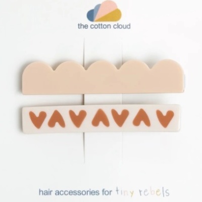 Dois acessórios para cabelo em tons neutros com padrões decorativos e texto da marca