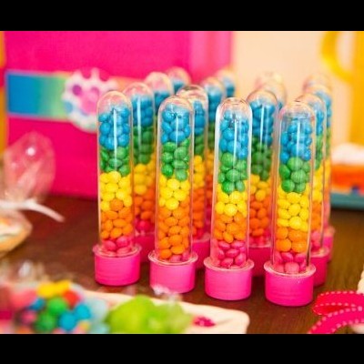 Tubo transparente com confeitos coloridos organizados em camadas, em cima de mesa colorida